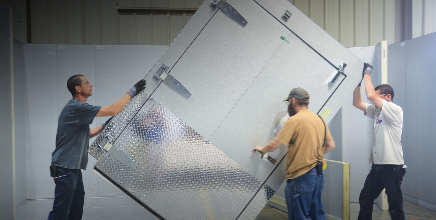 Three men carrying a walk in cooler door.