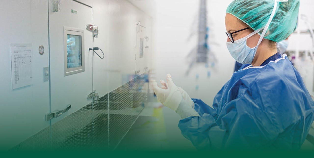 Woman in medical scrubs putting on gloves and standing in front of a walk in  cooler.